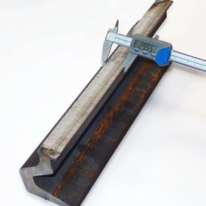 Suwmiarka cyfrowa mierząca średnicę metalowego pręta umieszczonego w żeliwnym uchwycie. Wyświetlacz pokazuje wartość 23.56 mm