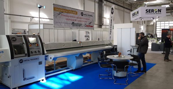 Stoisko wystawiennicze z maszyna CNC Metal Technika na niebieskiej podłodze, banner informacyjny, osoby odwiedzające targi pr