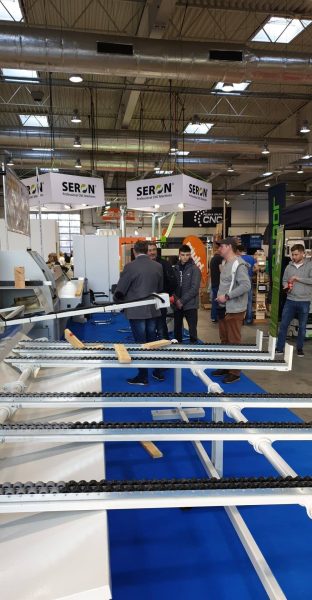 Targi przemysłowe w hali - stanowisko firmy Seron z maszynami CNC, wyposażeniem do obróbki drewna i odwiedzającymi zwiększają