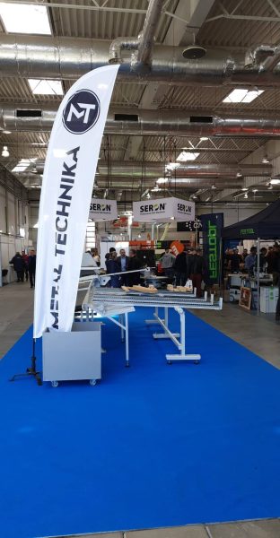 Stragan wystawienniczy marki Festool Technika w hali przemysłowej. Biały banner z logiem, niebieska podłoga, stół demonstracy