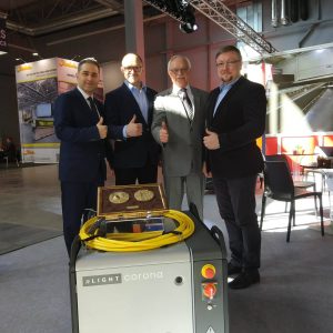 Czterech mężczyzn w garniturach przy urządzeniu nLight Corona CFX-5000 na targach przemysłowych. Wszyscy pokazują kciuki do g