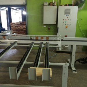 Przemysłowa linia produkcyjna z białymi przenośnikami łańcuchowymi, panelem sterowania, zieloną ścianą i oknami w tle.