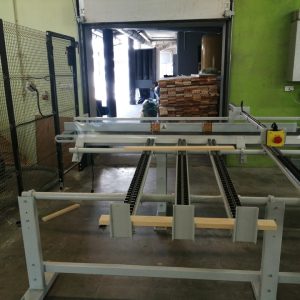 Wnętrze warsztatu z białymi maszynami do obróbki drewna, zieloną ścianą, metalową klatką po lewej i otwartymi drzwiami w tle.