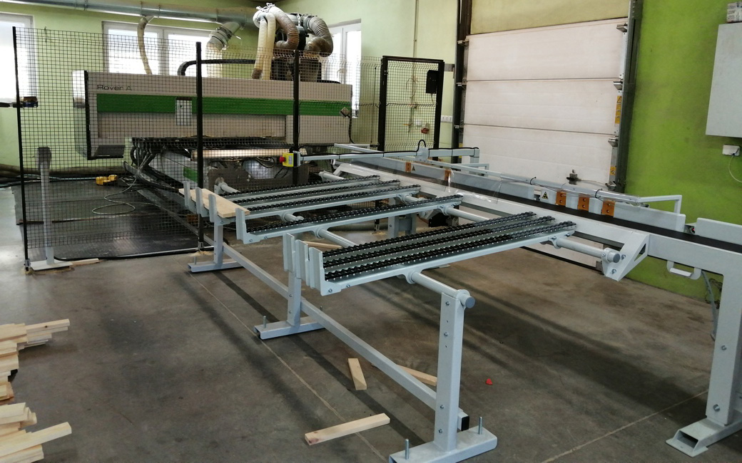 Hala produkcyjna z białymi stalowymi stołami transportowymi na kółkach, siatkowymi ogrodzeniami bezpieczeństwa i zieloną ścia