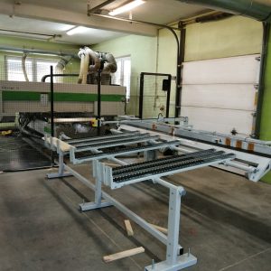 Warsztat produkcyjny z urządzeniami CNC, białymi stołami roboczymi z czarnymi przenośnikami, zieloną ścianą i ogrodzeniami be