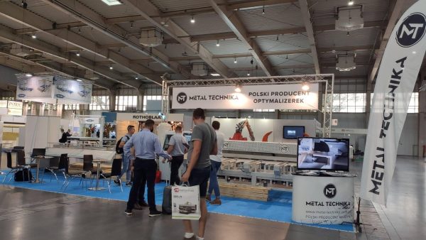 Stoisko firmy Metal Technika na targach w hali wystawienniczej. Ludzie oglądają maszyny i urządzenia metalowe. Baner reklamow