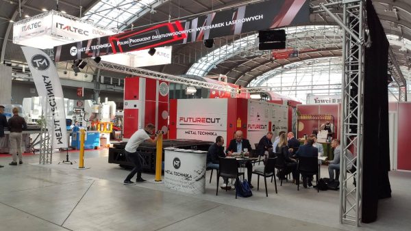 Targi przemysłowe w hali wystawienniczej. Stoisko Metal Technika z czerwono-białymi maszynami FutureCut, banner ITALTEC, osob